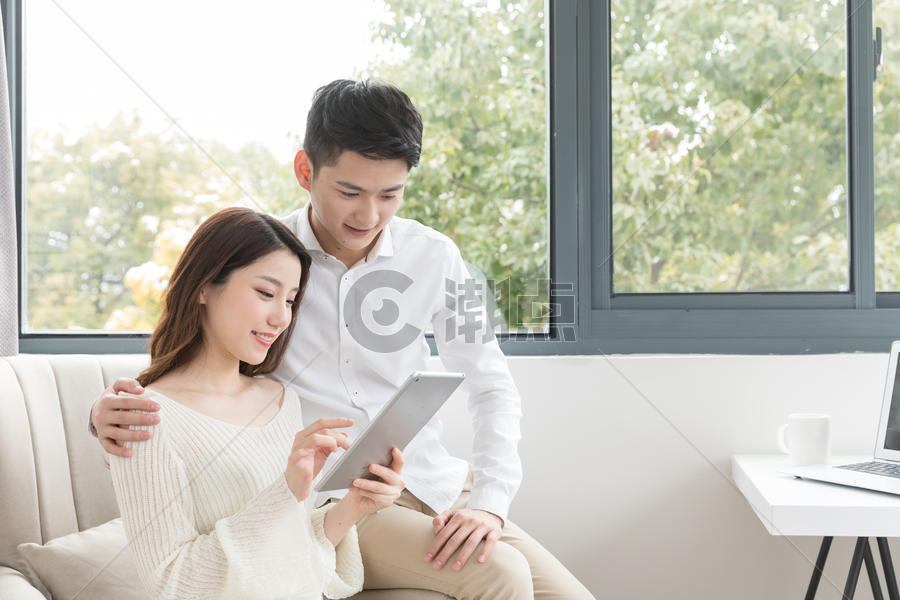 年轻夫妻幸福地坐在沙发上看平板电脑图片素材免费下载