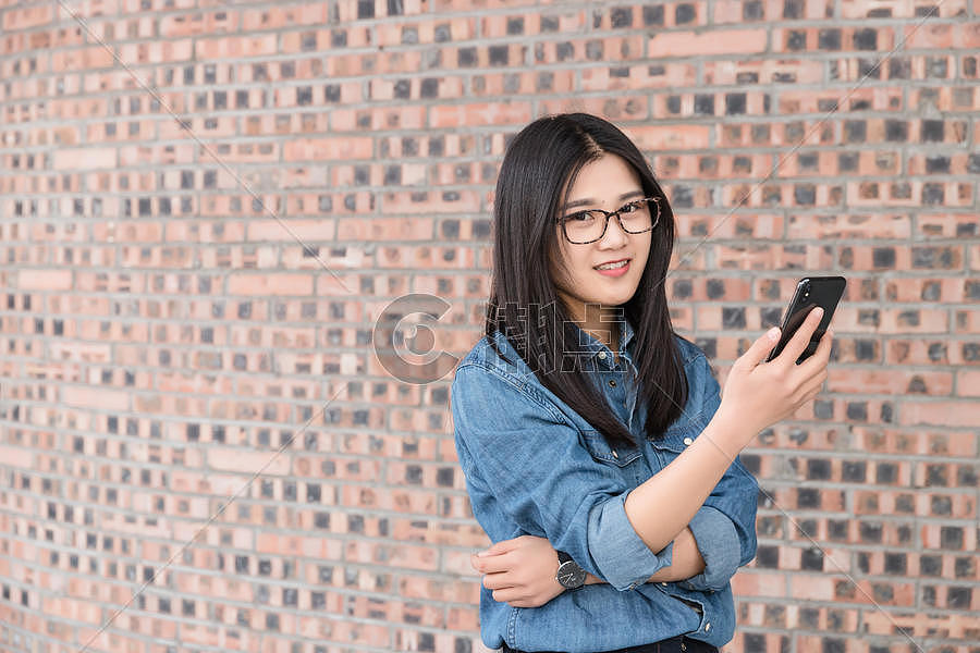 站在墙前的年轻女性用手机图片素材免费下载