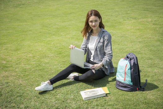 女学生在大学草坪上看电脑图片素材免费下载
