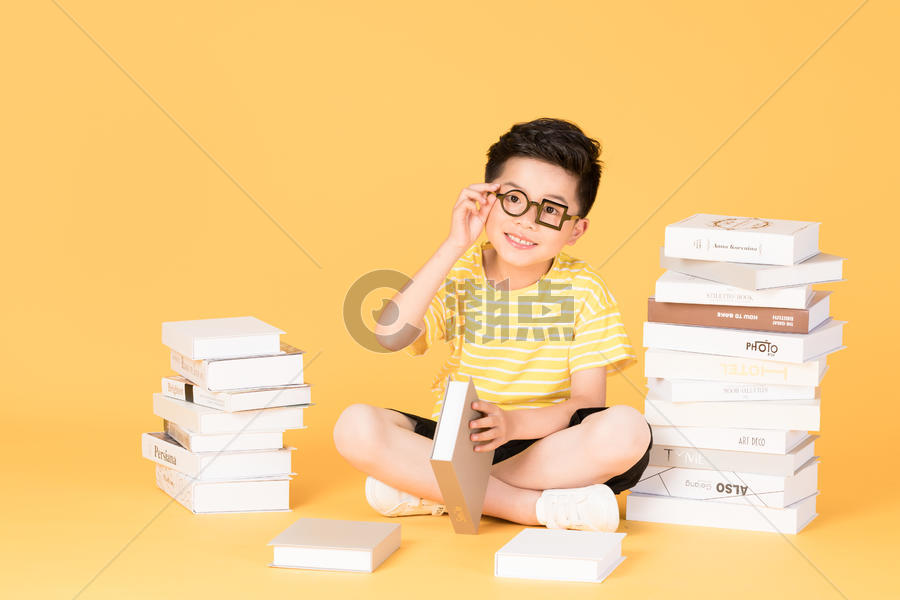 拿着书本坐在书旁的快乐男孩图片素材免费下载