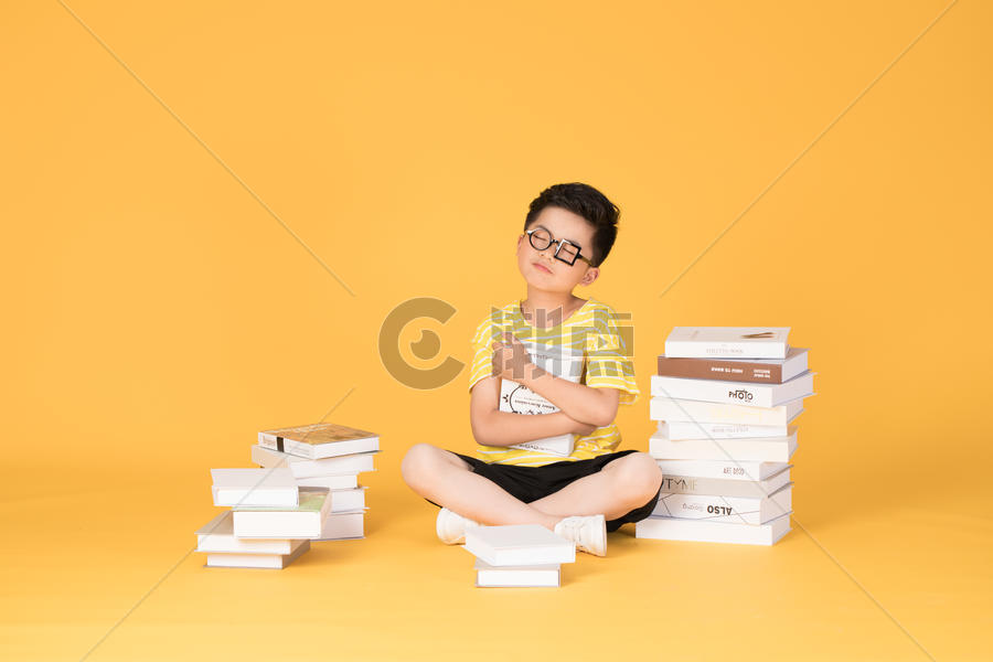 拿着书本坐在书旁的快乐男孩图片素材免费下载