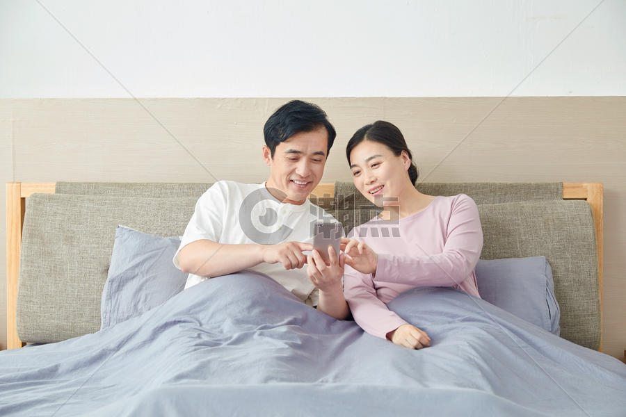 中年夫妇在床上玩手机图片素材免费下载