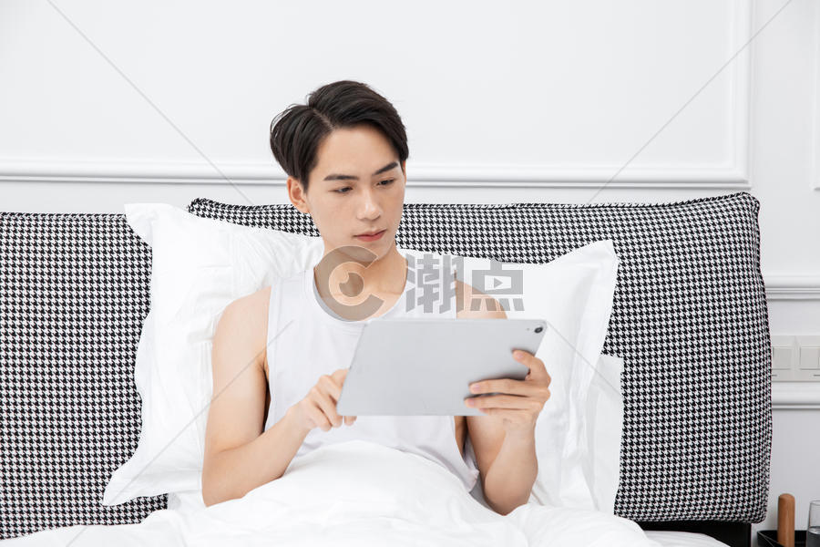 居家男青年床上玩平板电脑图片素材免费下载