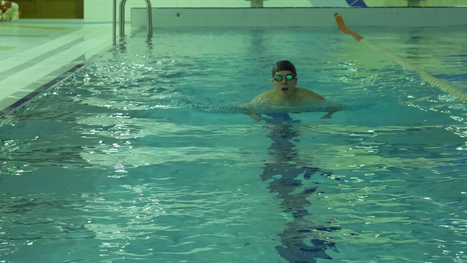 戴着帽子和护目镜的男子在游泳池里用蓝水游泳视频的预览图