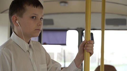 一个男孩乘公共汽车穿过城市近距离拍摄他听音乐视频的预览图