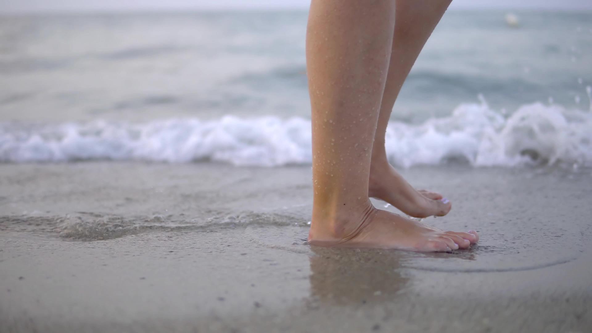 年轻女性在夏日海滩上沿着海水和沙子的潮流行走视频的预览图
