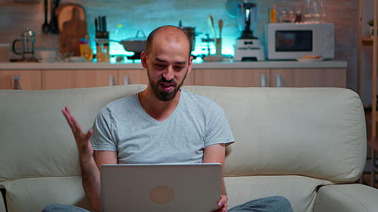 一名男子穿着睡衣坐在沙发上在笔记本电脑上工作视频的预览图