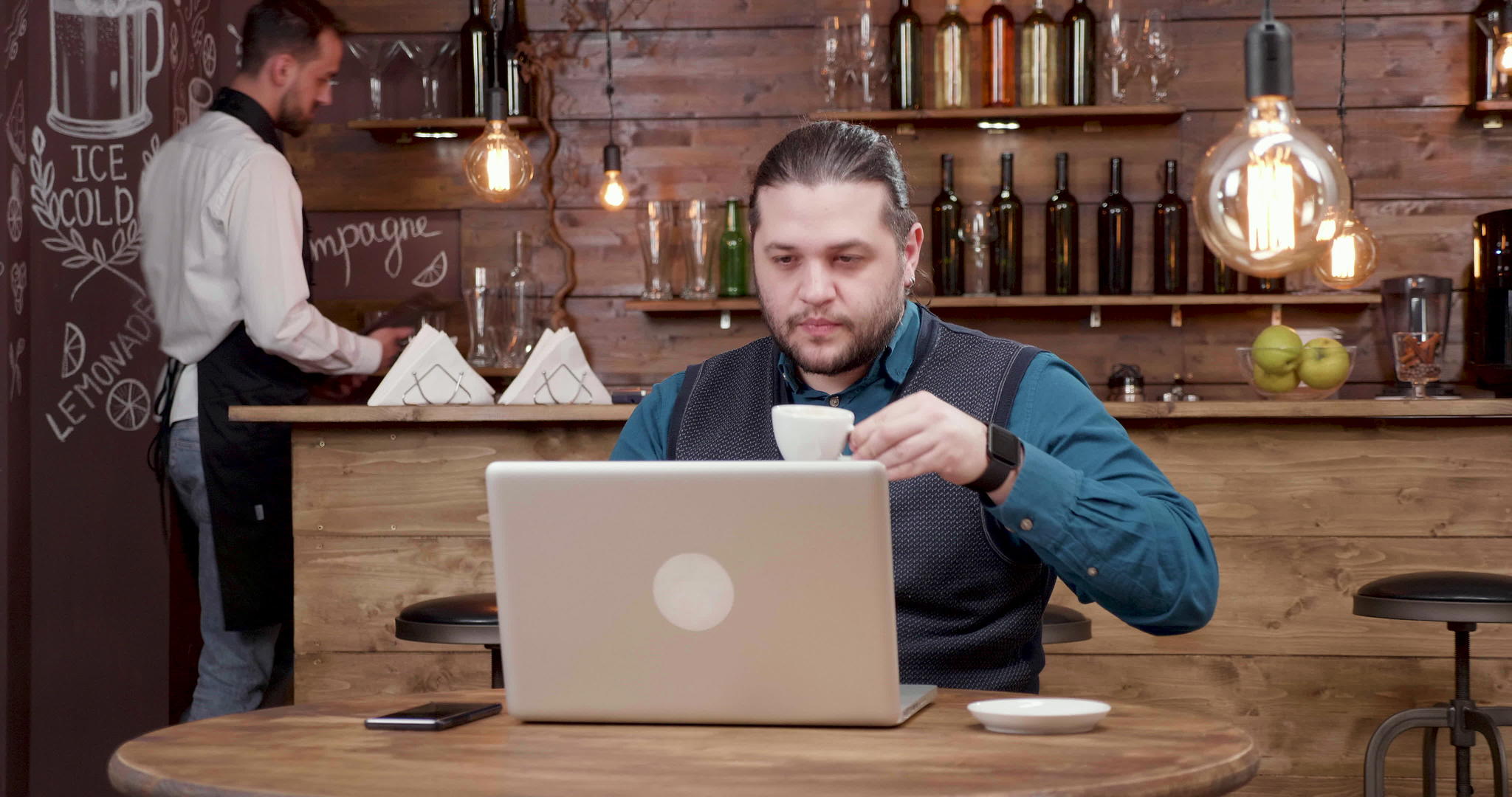 长发长发英俊的男人看着笔记本电脑屏幕喝咖啡视频的预览图