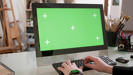 创意设计师在他的电脑上工作显示器上有一个绿色屏幕视频的预览图