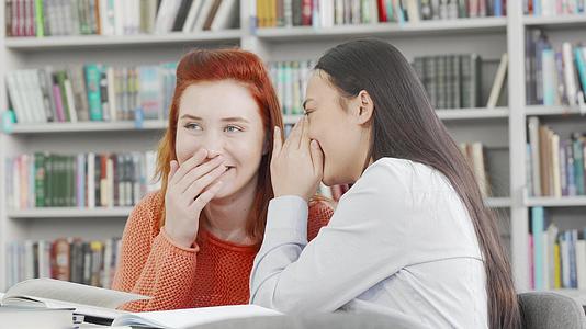女大学生朋友在图书馆里低语微笑着说话视频的预览图