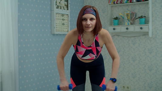 30多岁的年轻女性穿着运动服在家里用哑铃做健身运动视频的预览图