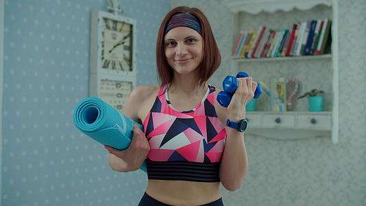 30多岁的年轻女性穿着运动服手里拿着哑铃和健身垫视频的预览图