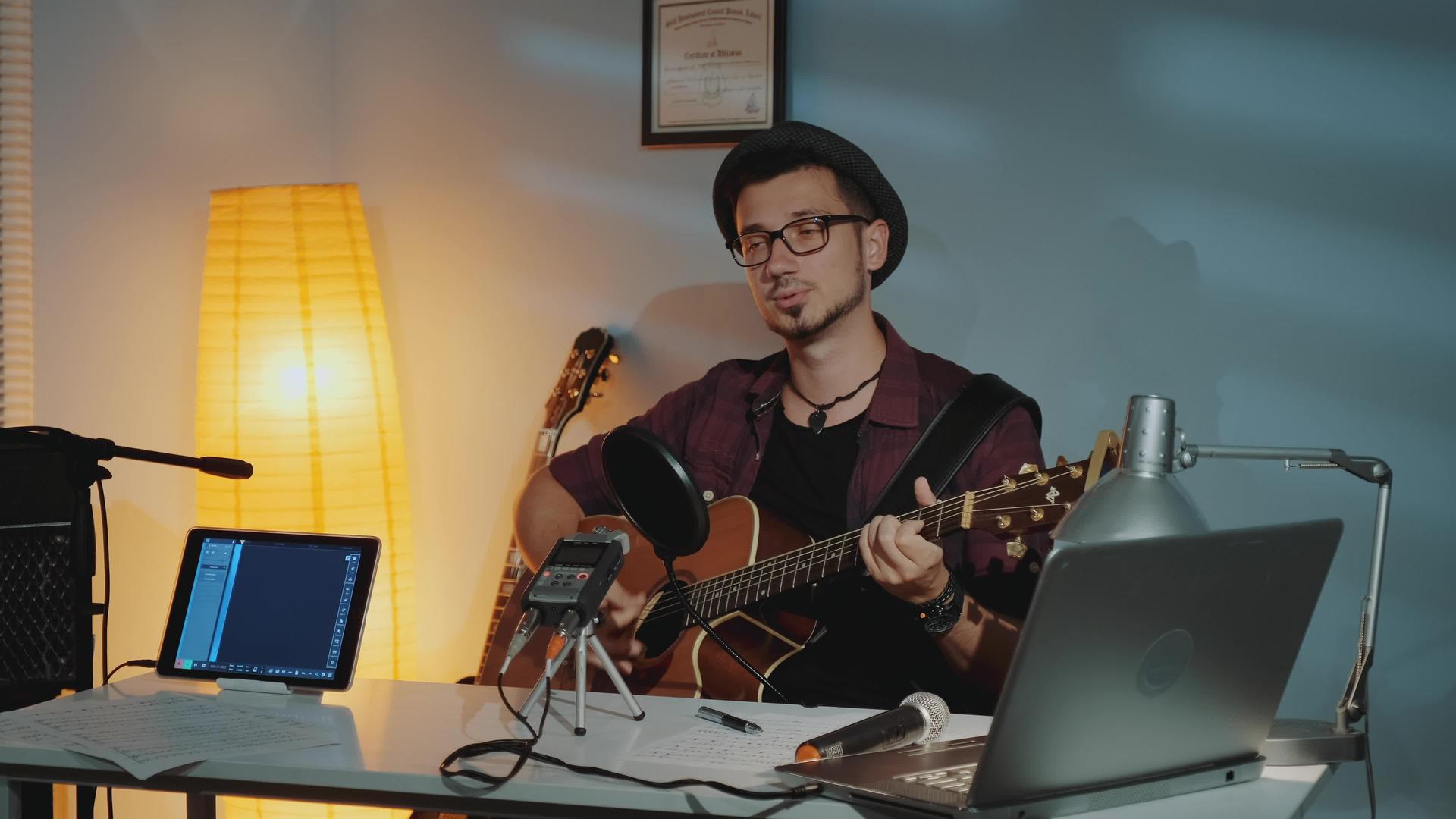 英俊的年轻音乐家在家庭工作室录制他的新曲目视频的预览图