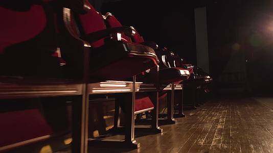 红色天鹅绒空座椅由戏剧厅低角度滑动的聚光灯照亮视频的预览图