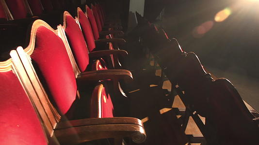 红色天鹅绒座位排成一排在空荡荡的剧院大厅里被聚光灯照亮视频的预览图