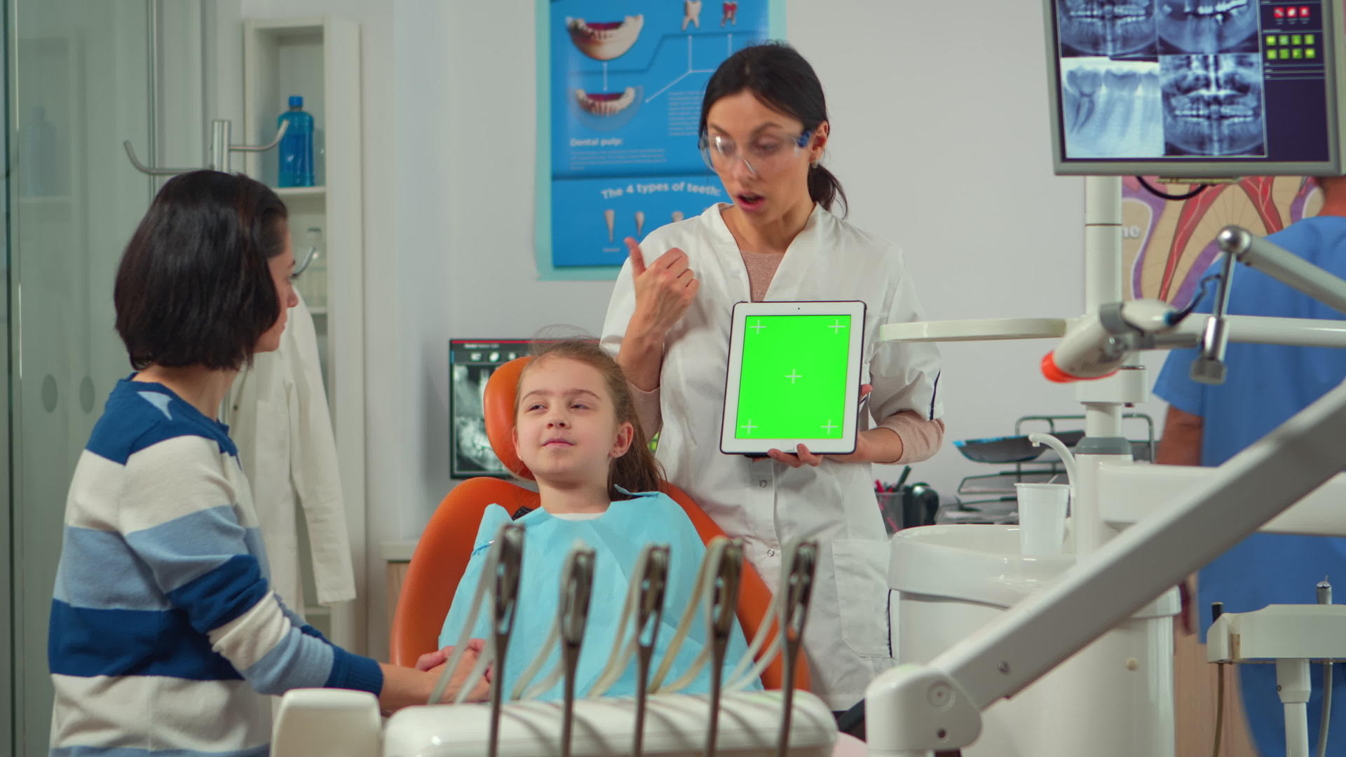 儿科牙医站在女病人旁边指着绿色屏幕显示器视频的预览图