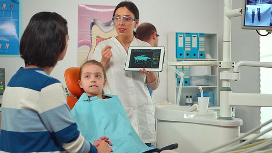 口腔科学家指向数字屏幕上向母亲解释X射线视频的预览图