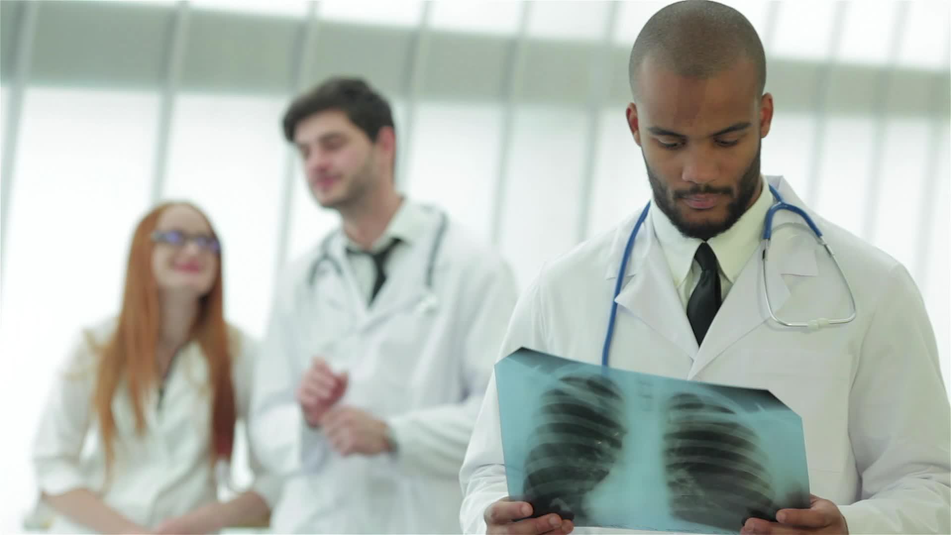 一位年轻医生的肖像照片两位同事的背景是X光片视频的预览图