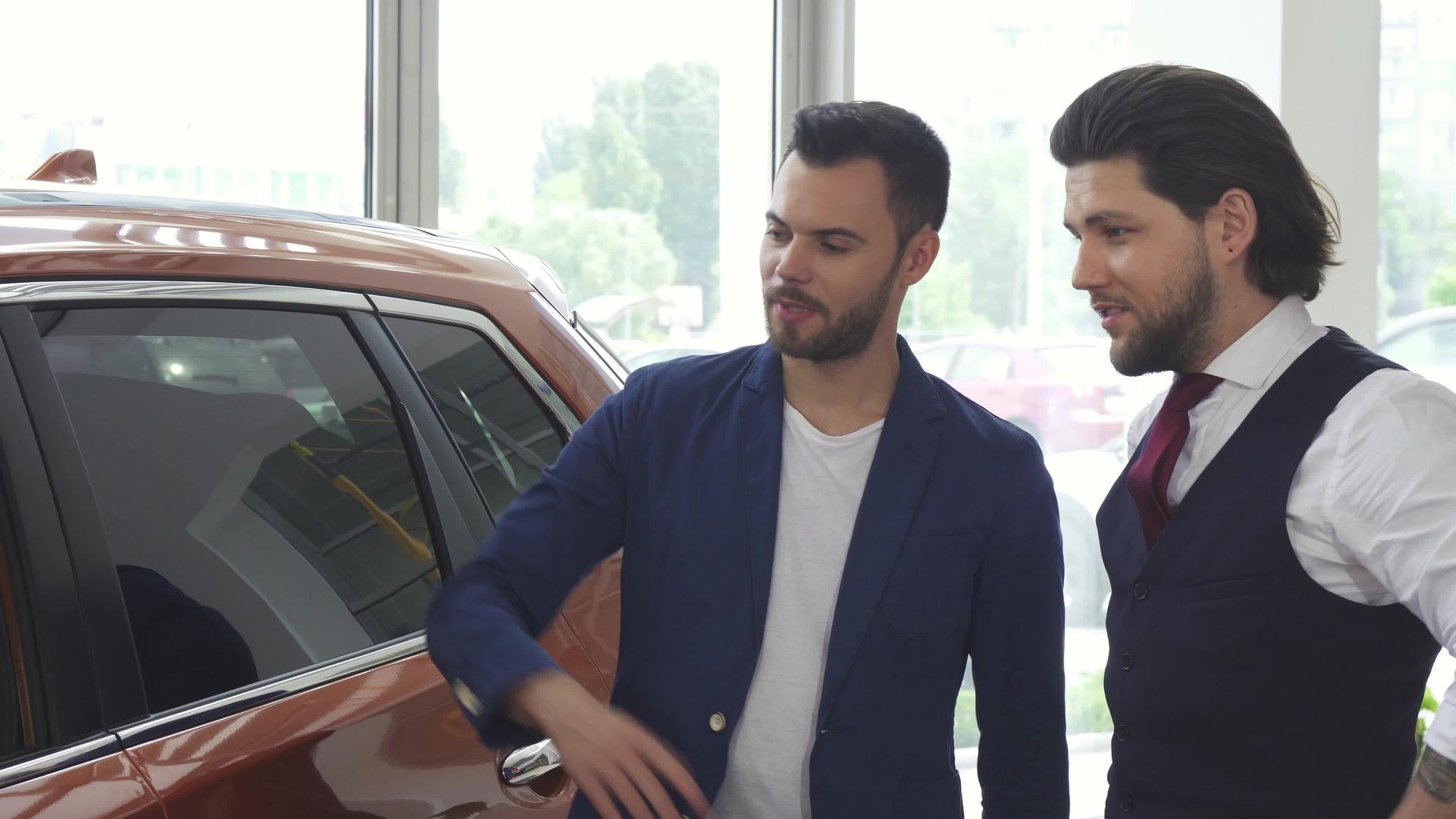 两个男性朋友在分销沙龙与一辆新车交谈视频的预览图