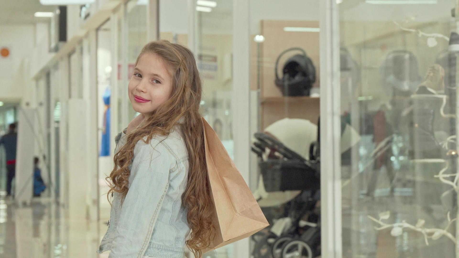 快乐的小女孩对着镜头微笑在商场里拿着购物袋视频的预览图