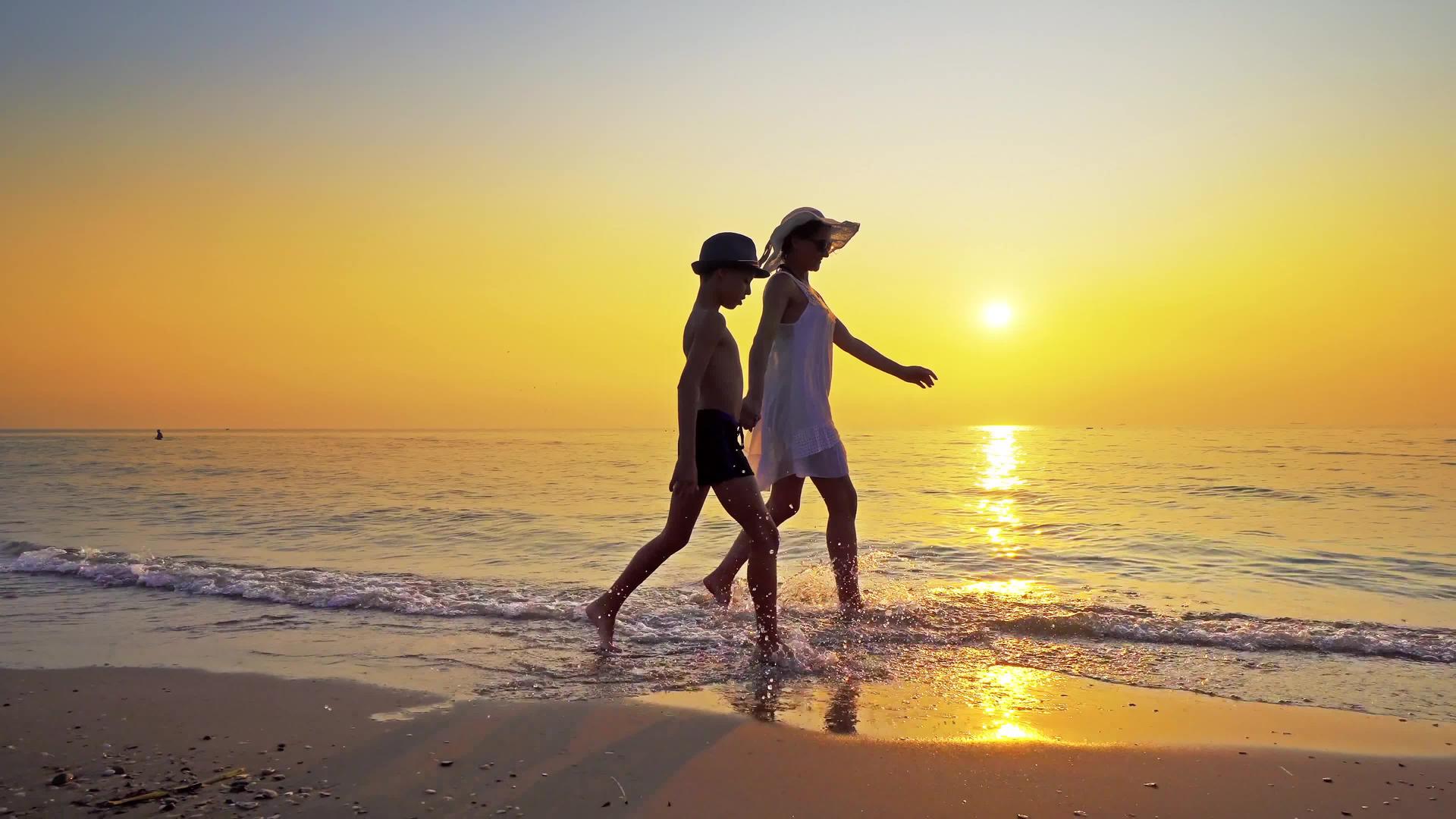 幸福的家庭在海边散步在日落时喷水踢浪妈妈穿白裙子穿白裙子视频的预览图