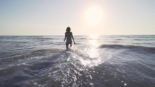 日落时穿着比基尼的女孩在海里行走视频的预览图