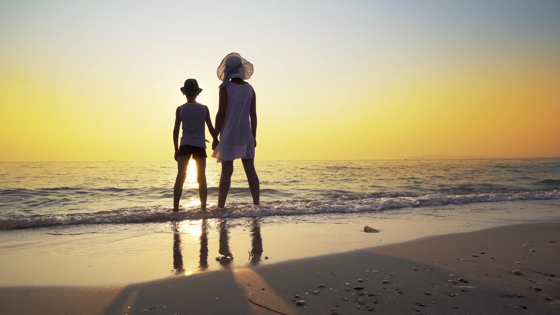 夏天在海上日落时分相爱的家庭抱着一位穿着白色连衣裙的母亲抱着她的小儿子视频的预览图