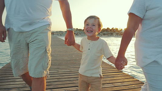 快乐的男孩在日落时和祖父母一起走在码头上视频的预览图