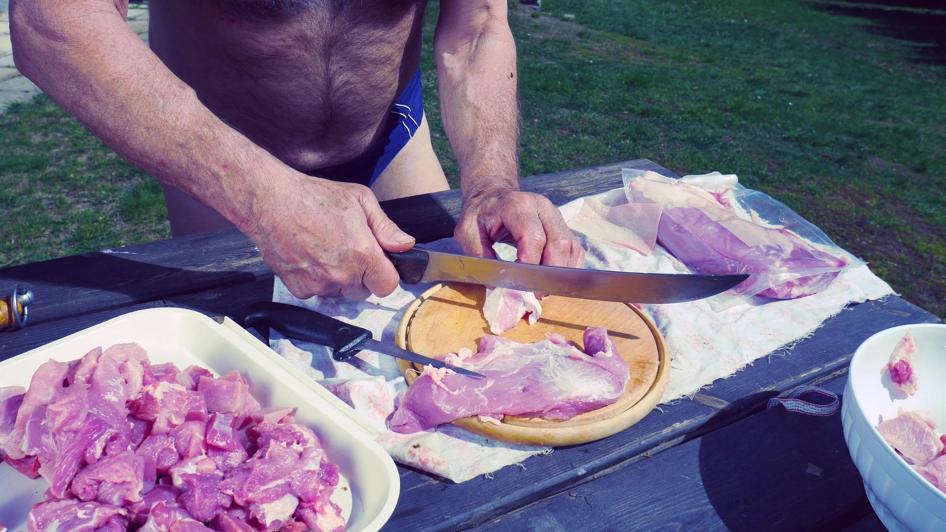 厨师正在用木板上的长屠宰刀切猪肉为菜园做饭视频的预览图