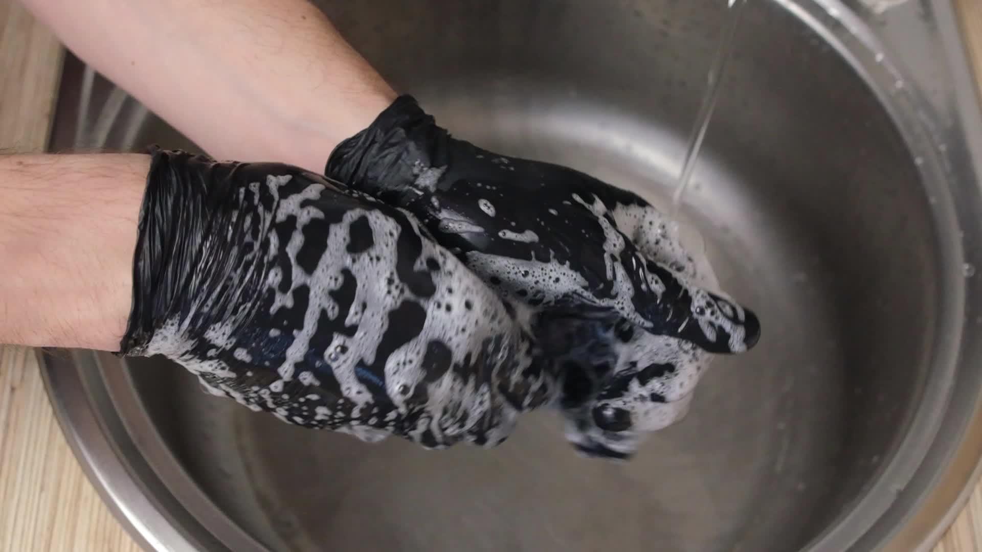 一名男子在水龙头下的水槽里用黑色橡胶手套洗手视频的预览图