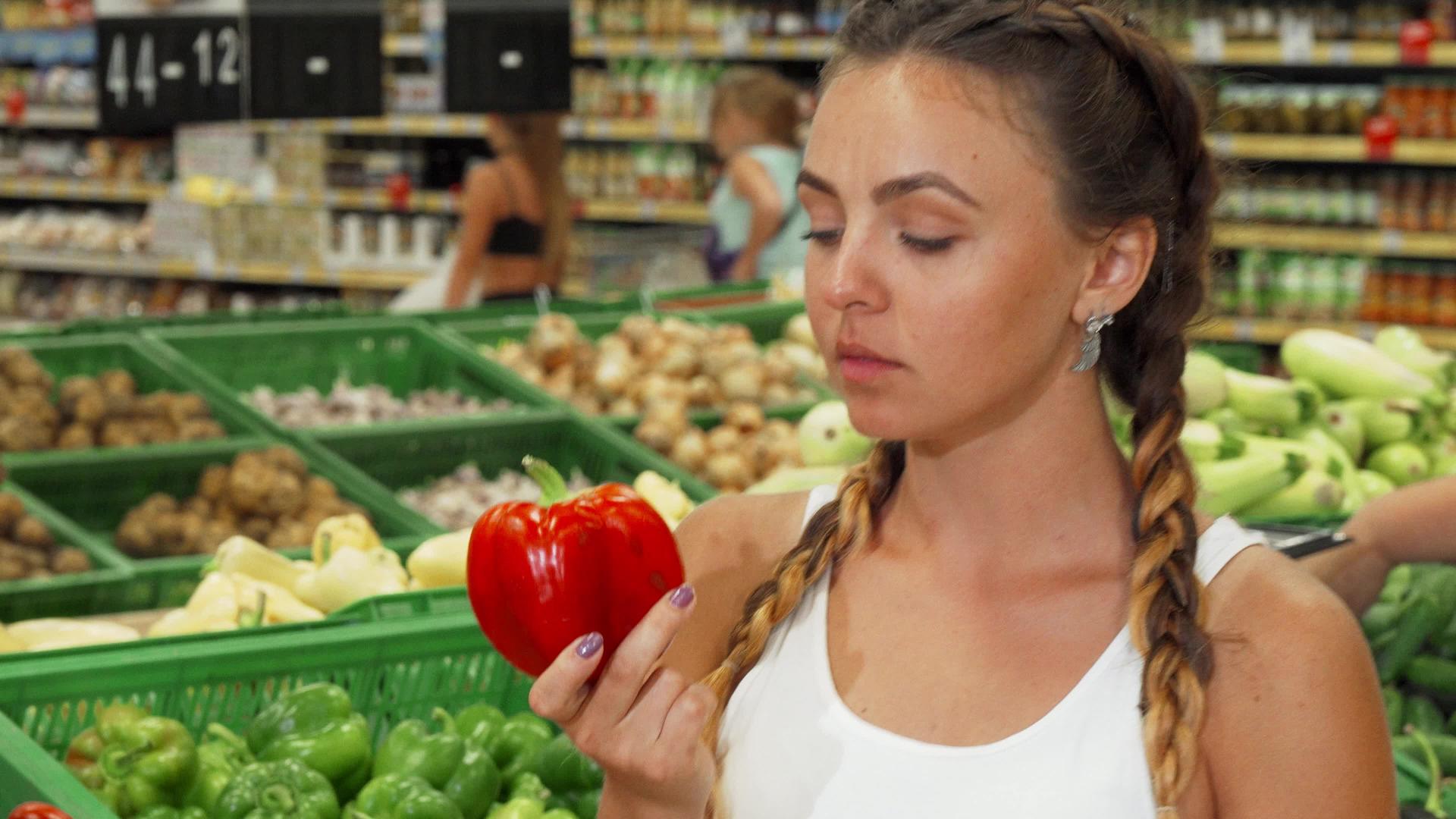 美丽的年轻美女闻到超市里辣椒的味道视频的预览图