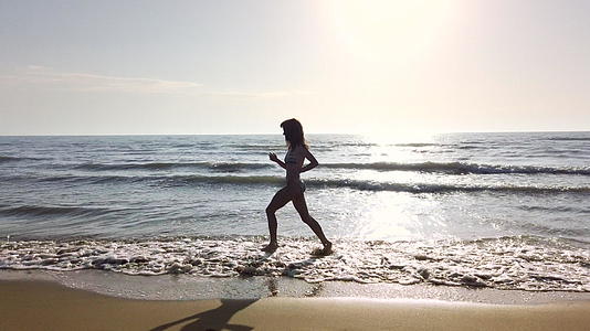 快乐美丽的双影女孩穿着比基尼日落时在海滩上奔跑视频的预览图
