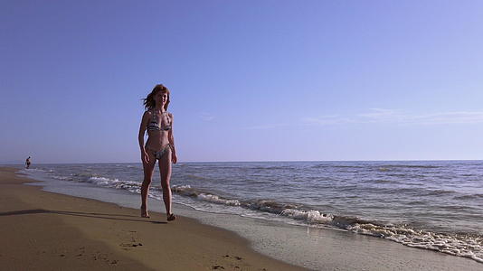 快乐美丽的女孩穿着比基尼日落时在海滩上奔跑微笑着视频的预览图
