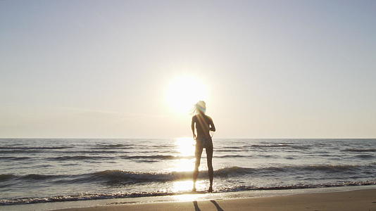 日落时穿着比基尼的月光女孩在海滩上快乐地跳舞视频的预览图