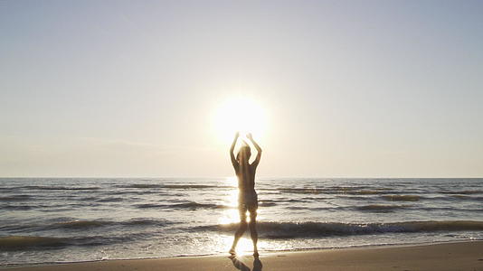 日落时穿着比基尼的月光女孩在海滩上快乐地跳跃视频的预览图