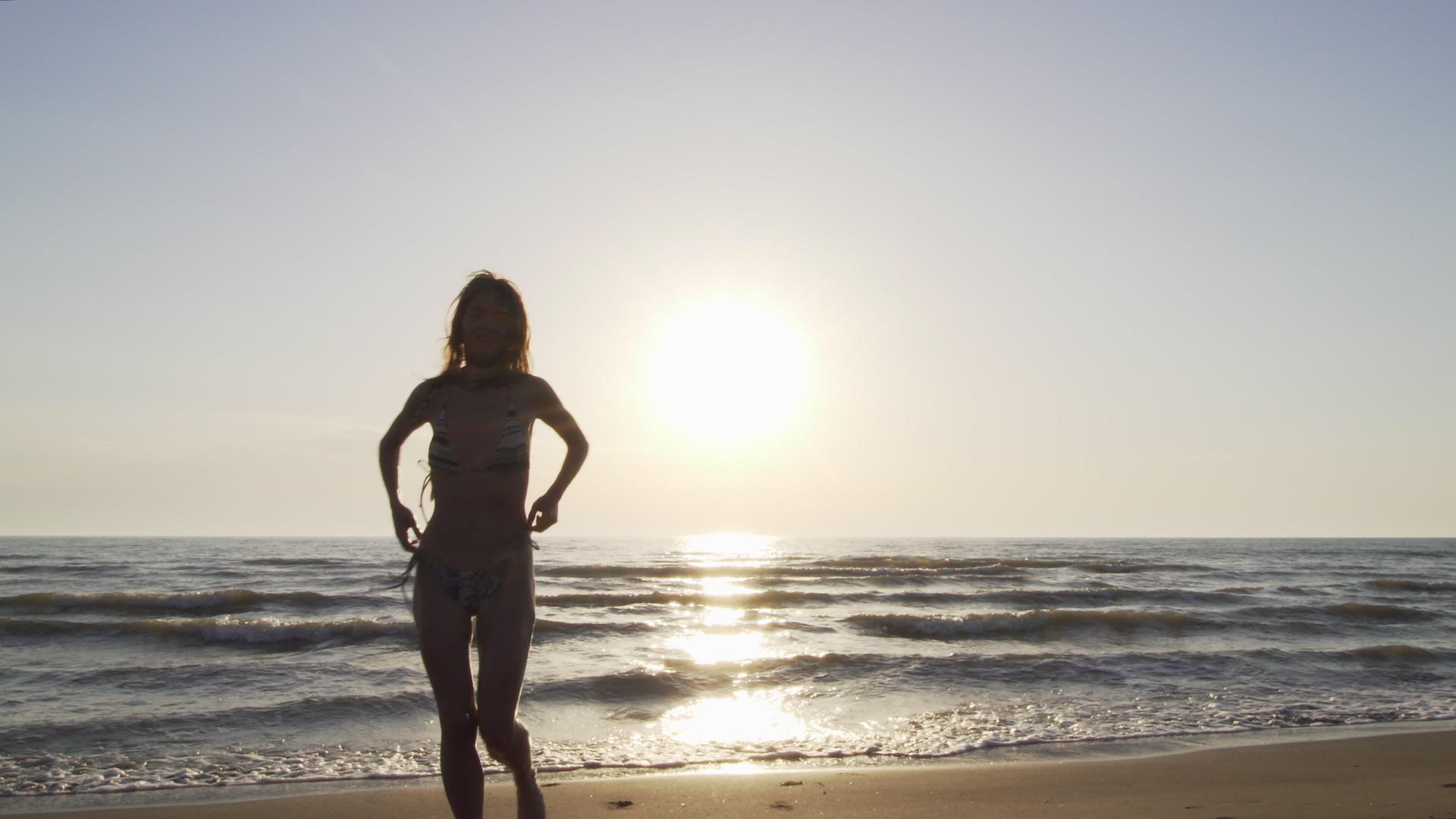 日落时穿着比基尼的月光女孩在海滩上跑向相机视频的预览图