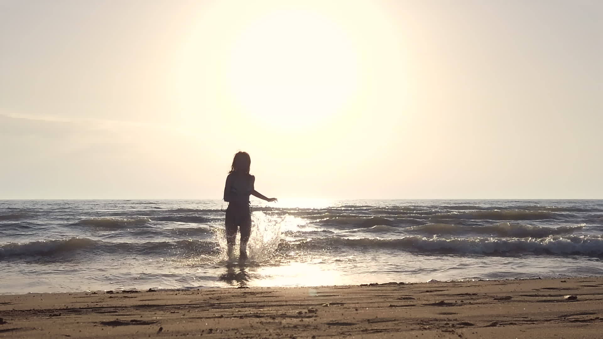日落时穿着比基尼的休眠女孩在海滩上跑向相机慢慢移动记录视频的预览图