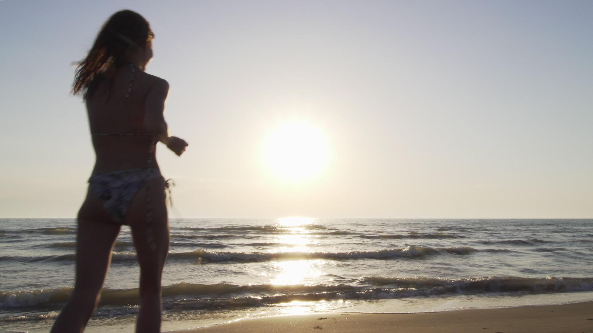 日落时穿着比基尼的月光女孩在海滩上跳跃视频的预览图