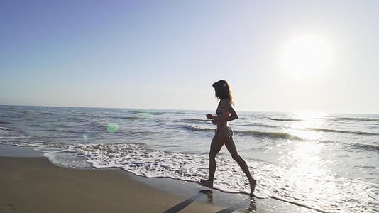 日落时穿着比基尼的女孩在海滩上奔跑视频的预览图