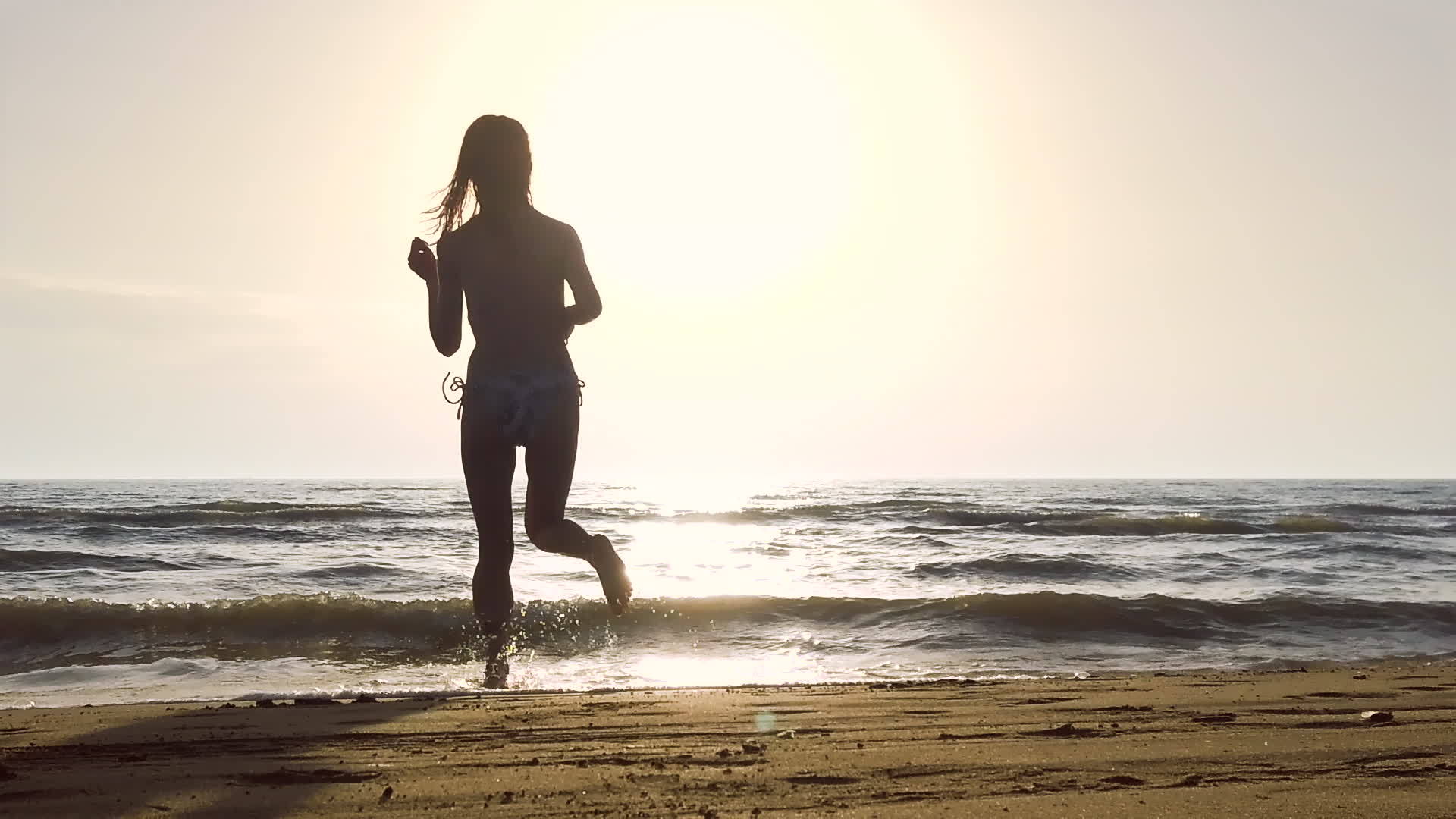 日落时穿着比基尼的女孩在海滩上跳跃视频的预览图