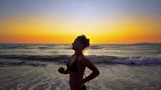 穿着比基尼的女人的轮廓在海滩上奔向日落电影制片人Standicam视频的预览图