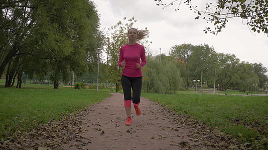 年轻的白人妇女在绿色的城市公园里慢跑在相机里落叶视频的预览图