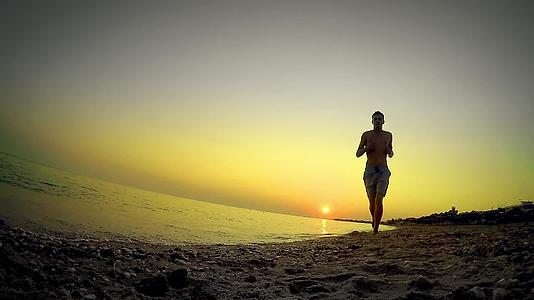 孤独的运动员在空旷的海边慢跑与日落相反视频的预览图