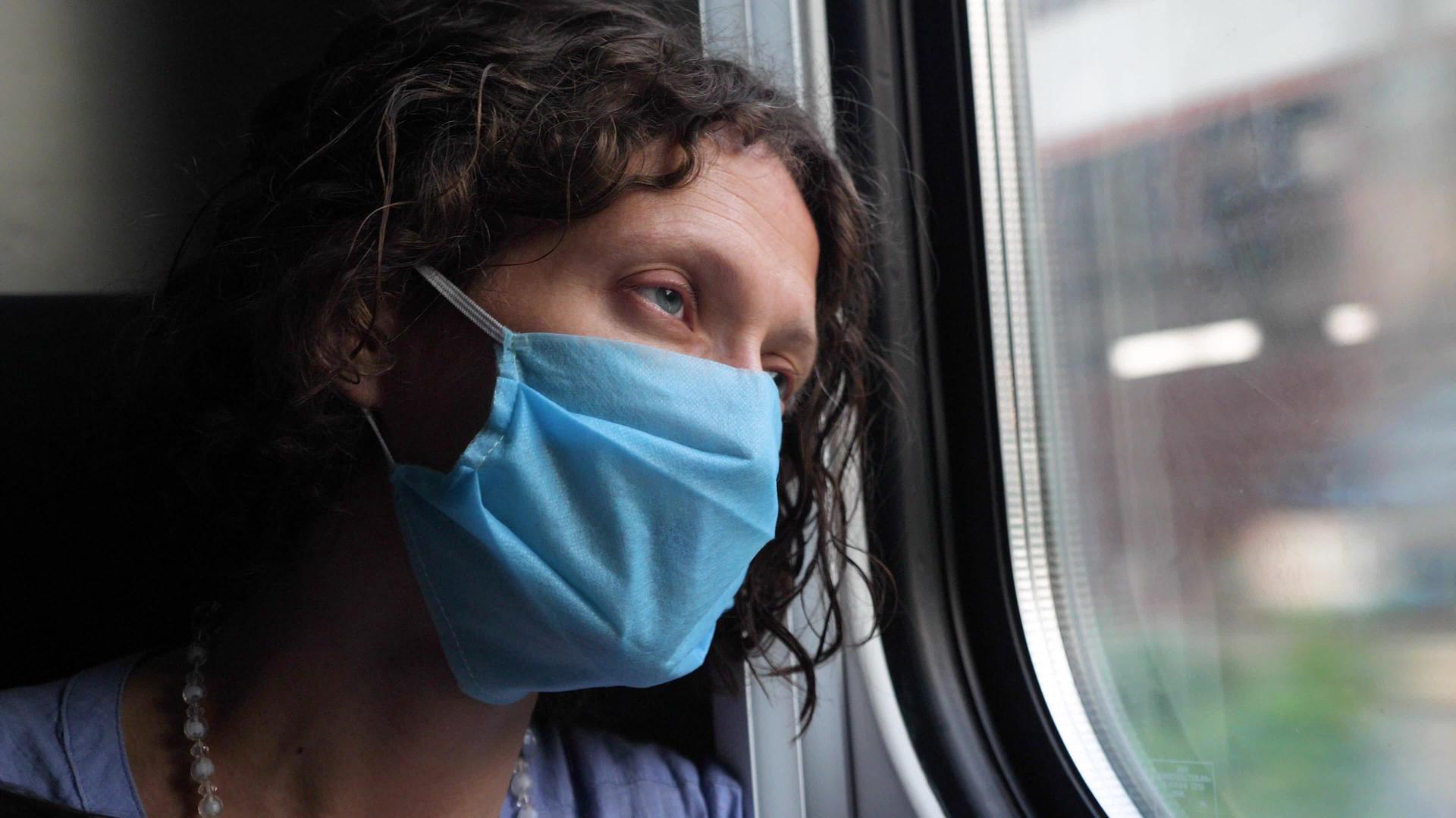 一个戴着蓝色防护面罩的疲惫的中年妇女看着火车窗外的火车窗视频的预览图