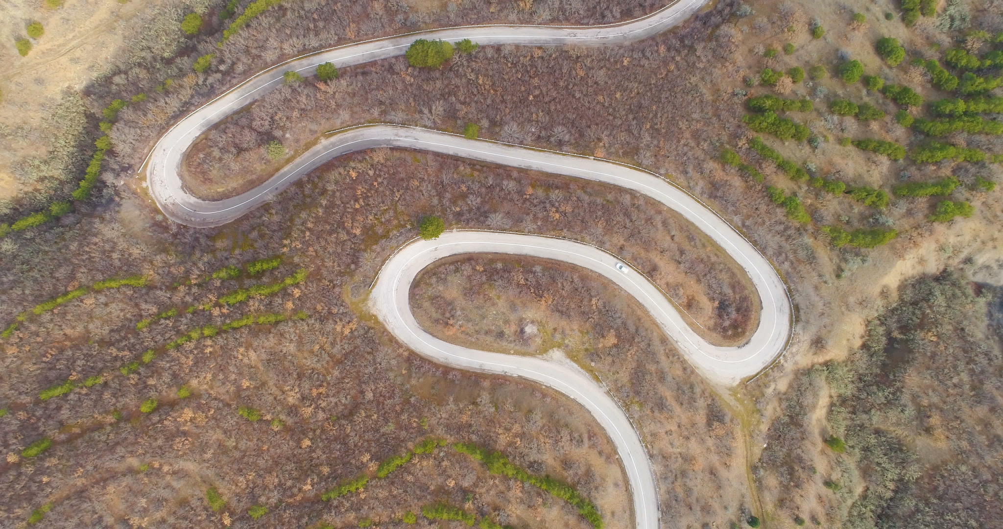 白色的汽车在蛇纹山路上飞行在绿色的山丘上飞行在空中视线最高视频的预览图