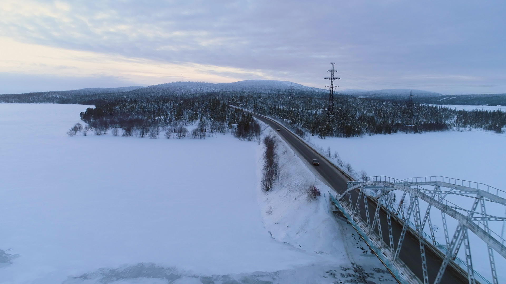 汽车在日落时在冬天的路上行驶冰冻湖上的桥鸟瞰机视频的预览图