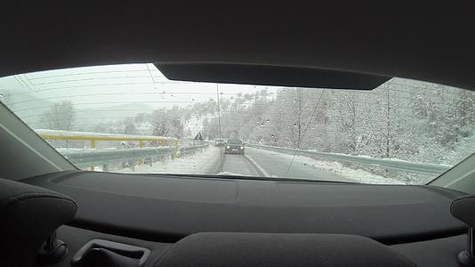 在冬在雪地里开车在雪地覆盖的雪山路上行驶穿过后挡风玻璃视频的预览图