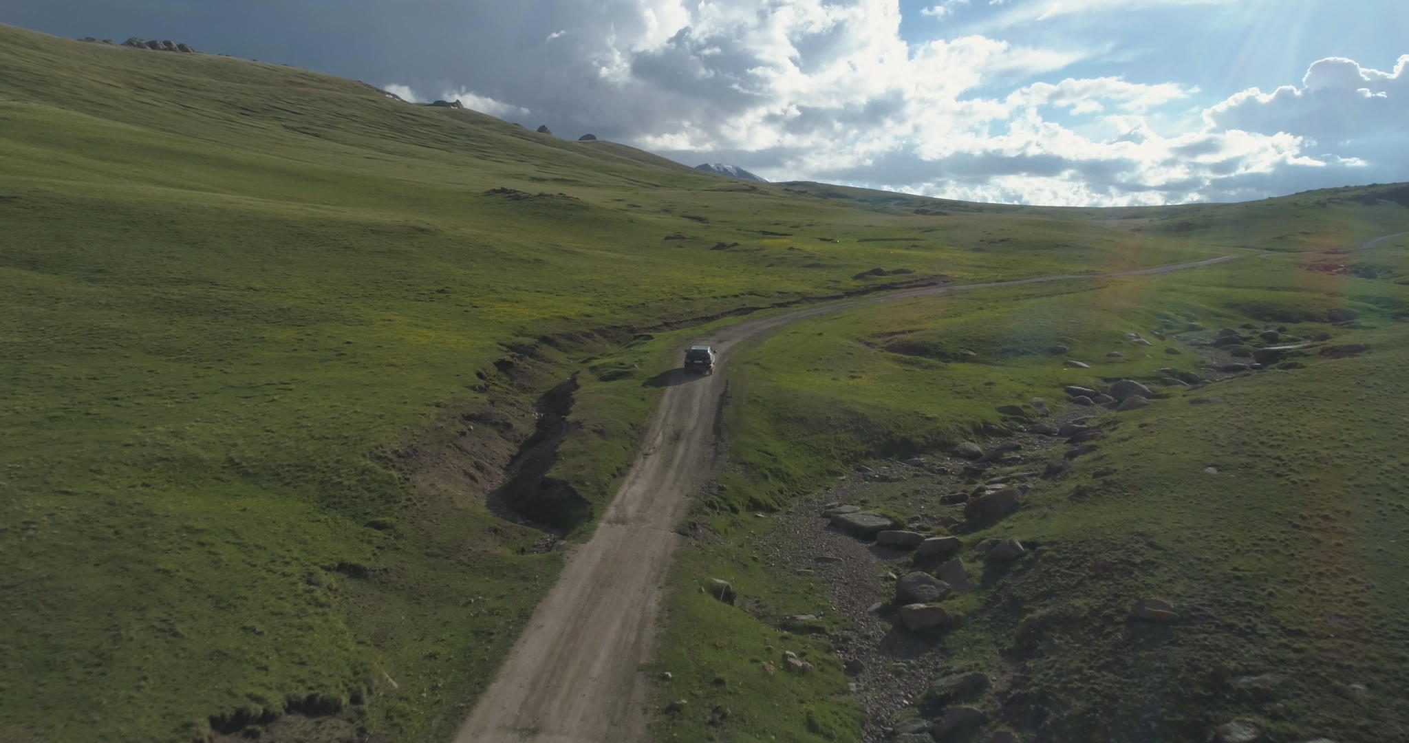 SUV汽车在夏天的绿色山丘上沿着碎石路行驶在空中观察无人驾驶视频的预览图
