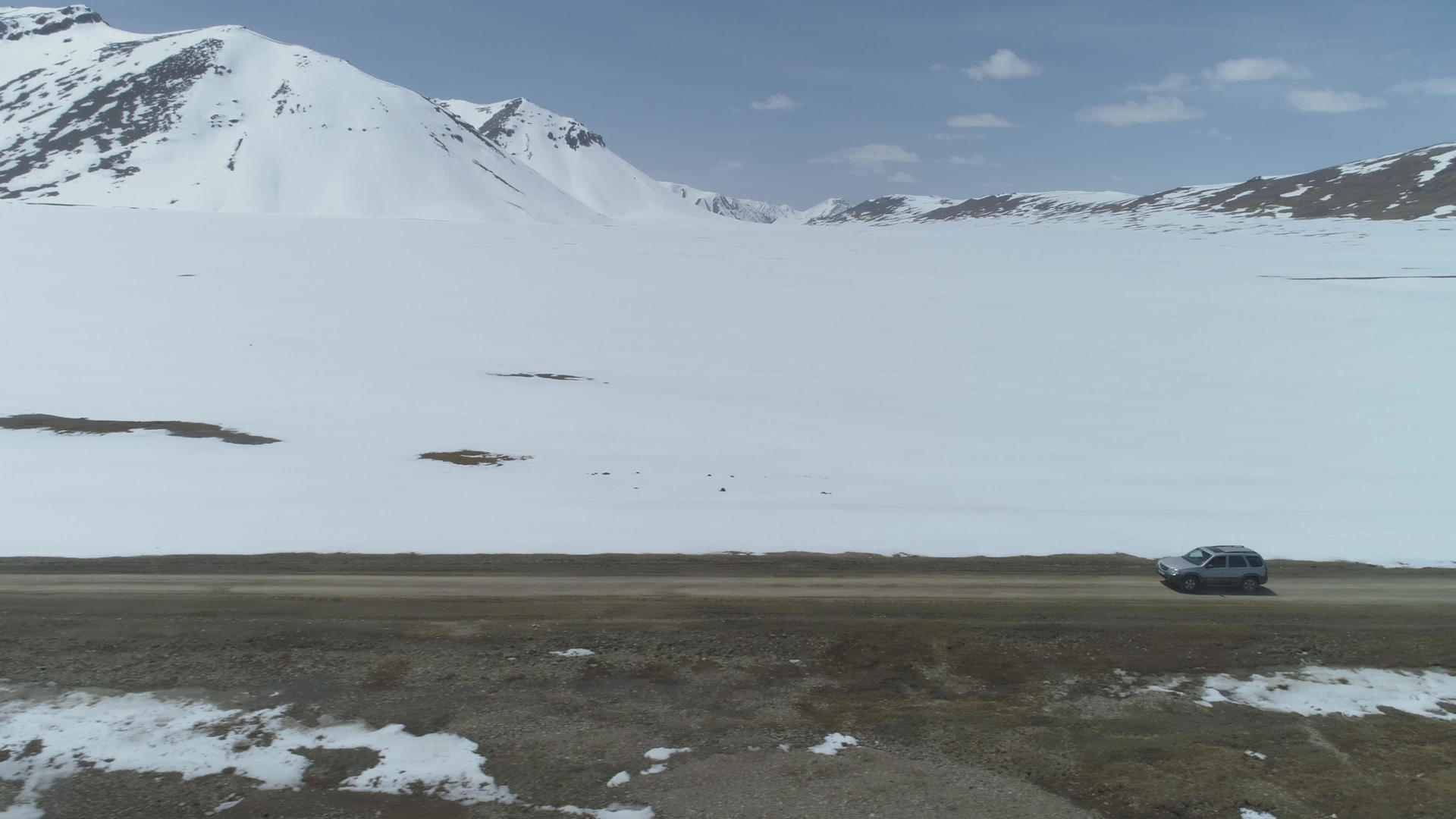 SUV在阳光明媚的白天汽车在雪山高海拔的砾石路上行驶视频的预览图