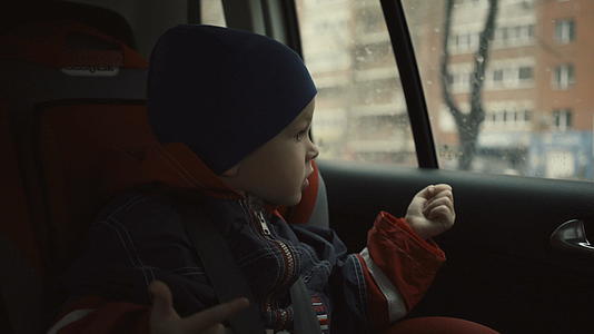 男孩坐在儿童座位的车里在雨季看着窗外视频的预览图